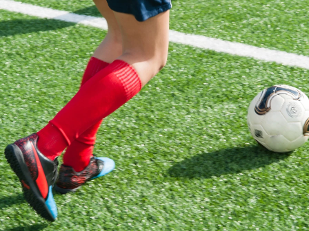 A close-up of a soccer player in red socks and cleats kicking a white soccer ball on green turf, near a white line, action shot.