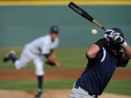 A baseball batter swings at the ball as a pitcher throws in the background on the field.