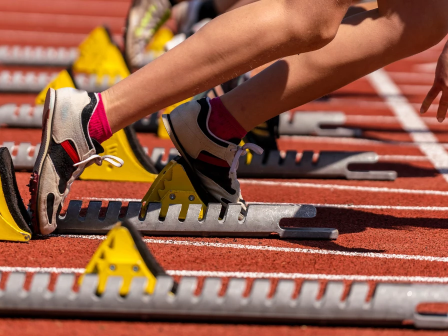 People sprinting off blocks at a track meet, starting gun ready, colorful shoes, orange track, and starting blocks lined up &mdash; go!