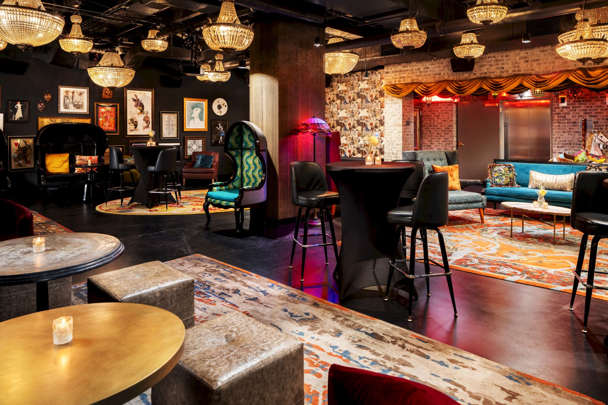 A trendy lounge/bar with velvet chairs, chandeliers, low seating, neon accents, and art on dark walls in a cozy, upscale setting.