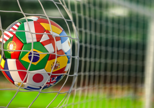 A colorful soccer ball with flags from Portugal, Brazil, Japan, and more, caught in a goal net against a green field, symbolizing international football.