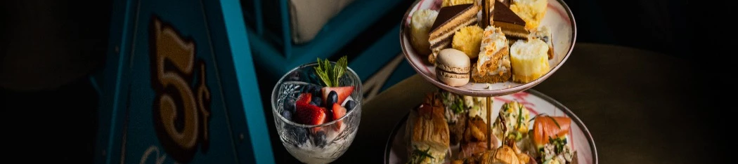 A four-tier tea-time stand piled with pastries, scones, and bites, plus a small cup of tea and a berry dessert on the side, elegant and cozy.