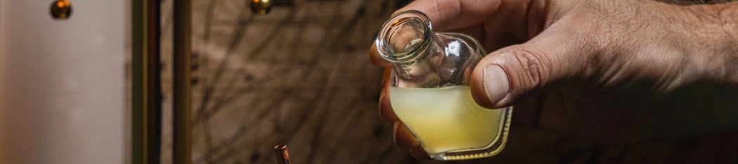 A bartender pours a lime wedge into a short glass with blue cocktail, while a hand squeezes a lemon over a drink, in a cozy bar.