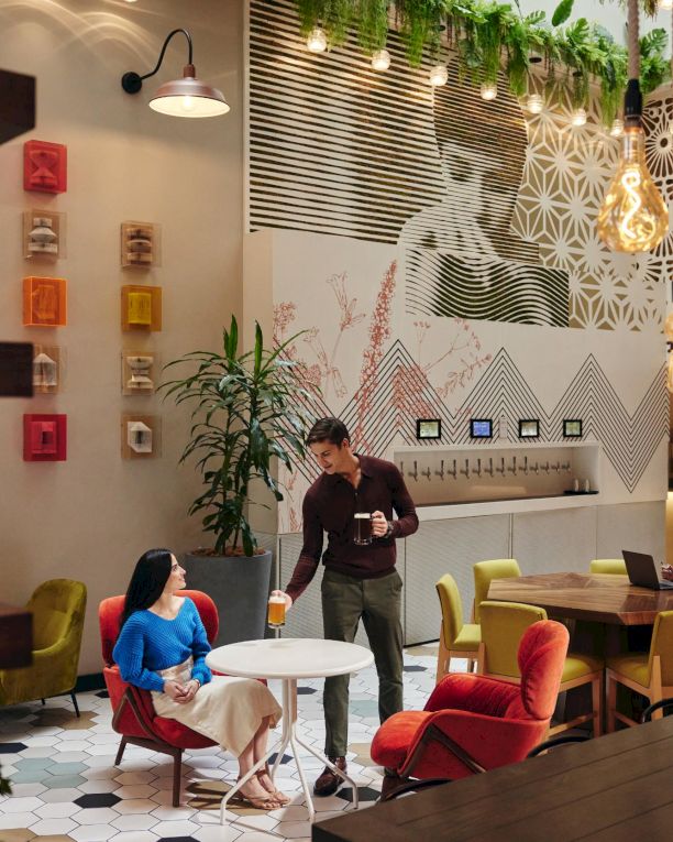 A modern coworking cafe with colorful chairs, hanging lights, plants, and people chatting and working on laptops. End.