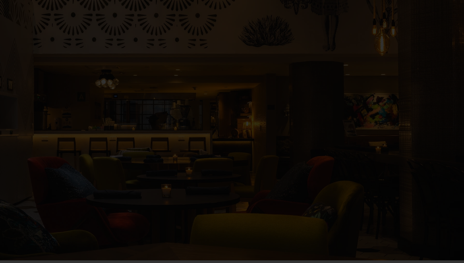 A dim, cozy lounge with plush chairs, low tables, warm lighting, and a modern bar area in the background, creating a relaxing ambiance.