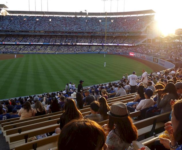 A crowded stadium with a sunny baseball field, fans seated and enjoying the game, warm evening light shining over the stands.