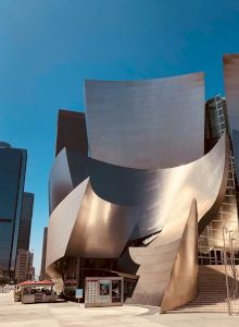 A futuristic metallic sculpture or architectural facade with curved, reflective metal panels against a blue sky, forming an abstract, modernist shape.