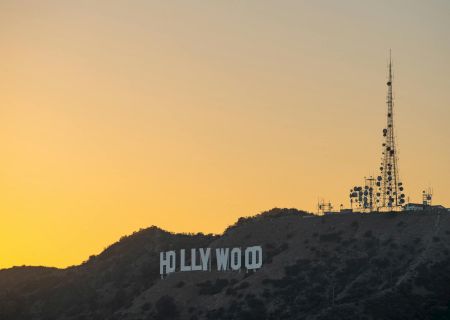A hillside at sunset with a distant sign and a tall antenna tower, silhouetted against a yellow-orange sky.